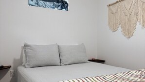 Un dormitorio con una cama, un adorno de macramé en la pared y una ventana pequeña.