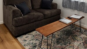 Una sala de estar con un sofá marrón, dos cojines negros, una mesa de centro de madera y una alfombra estampada.