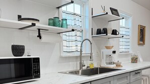 Une cuisine moderne avec des meubles blancs, un four à micro-ondes encastré, un évier et une machine à café.
