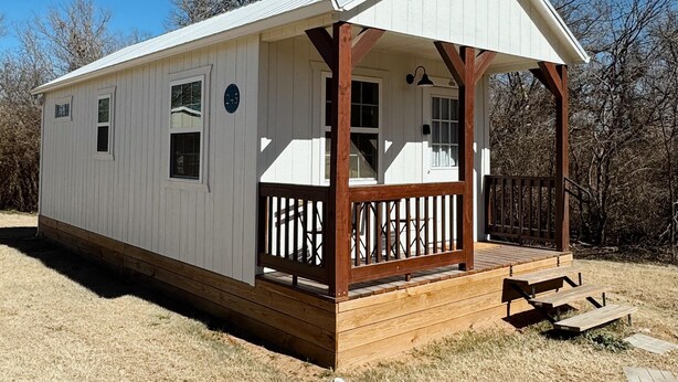 A small, single-story cabin with a covered porch and wooden deck.