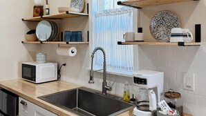 A modern kitchen with a sink, microwave, coffee maker, and various decorative items on shelves.