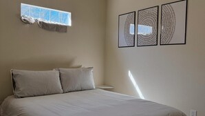 A bedroom with a bed, a ceiling fan, a window with a view, and three framed artworks on the wall.