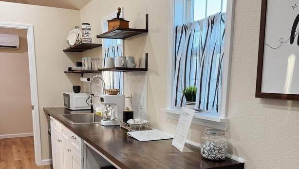 Een keuken met een houten aanrecht, witte kastjes en een raam met gordijnen.