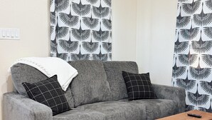 Een grijze bank met twee zwart-wit gestreepte kussens, een houten salontafel en een zwart-wit gestreept vloerkleed.