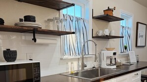 Een moderne keuken met witte kasten, een donker aanrecht, een magnetron, een spoelbak en een koffiezetapparaat.