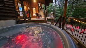 A hot tub with a wooden deck and a view of a forest.