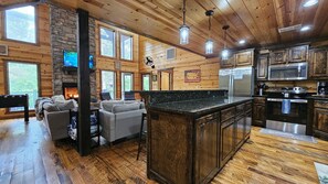 A cabin interior with a fireplace, wooden walls, a kitchen with modern appliances, and a cozy seating area.