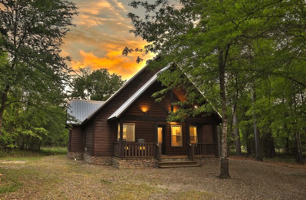 Une cabane rustique avec des fondations en pierre, un revêtement extérieur en bois et une véranda dotée d’une balustrade.
