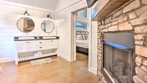A modern bathroom with a stone fireplace, white cabinetry, and two mirrors. - Romantic King Retreat:Hot Tub-Firepit-Deck-Dogs-Sleeps4 (Broken Bow)