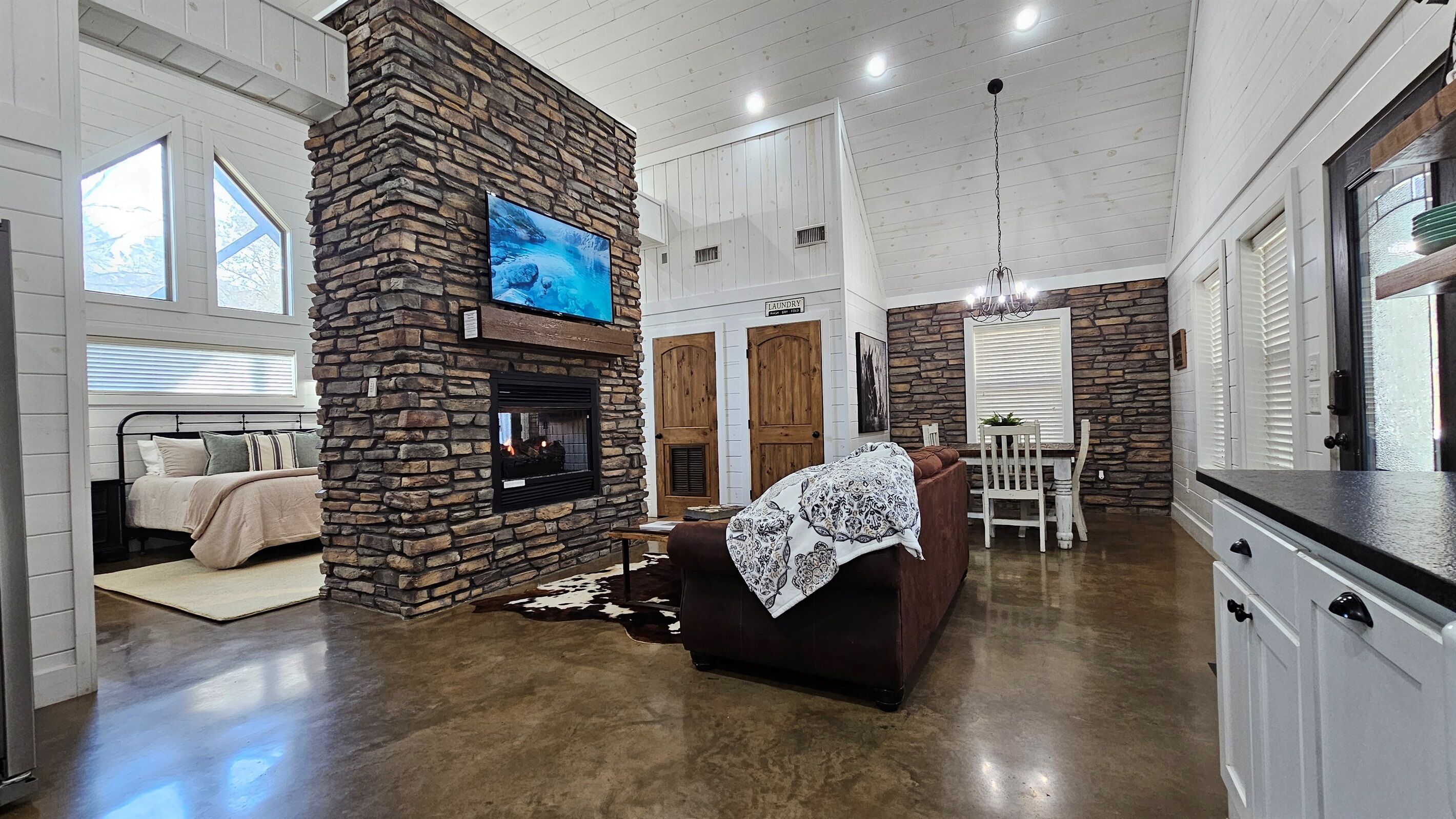 Amplia sala de estar con chimenea de piedra, televisor montado en la pared, mesa de comedor con sillas y zona de cocina con armarios.