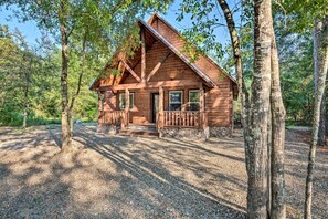 Une cabane en bois dotée d’un porche et reposant sur des fondations en pierre, entourée d’arbres.