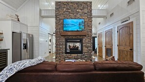 A spacious interior with a stone fireplace, a mounted television, and a brown leather couch. - Romantic King Retreat:Hot Tub-Firepit-Deck-Dogs-Sleeps4 (Broken Bow)