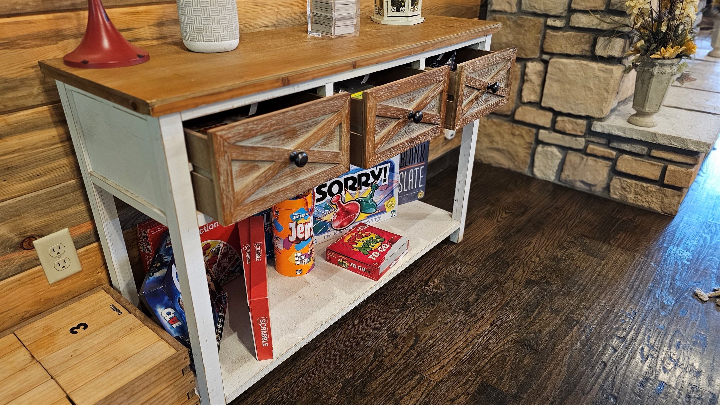 A wooden console table with drawers, a red lamp, and various board games.