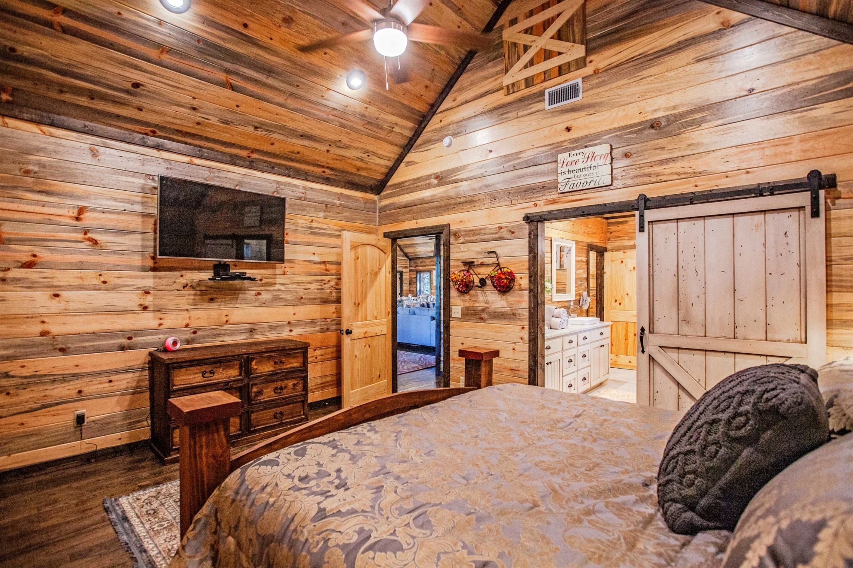 Ein Holzhütten-Interieur mit einem großen Bett, einem an der Wand montierten Fernseher und einer Schiebetür im Bauernhausstil.