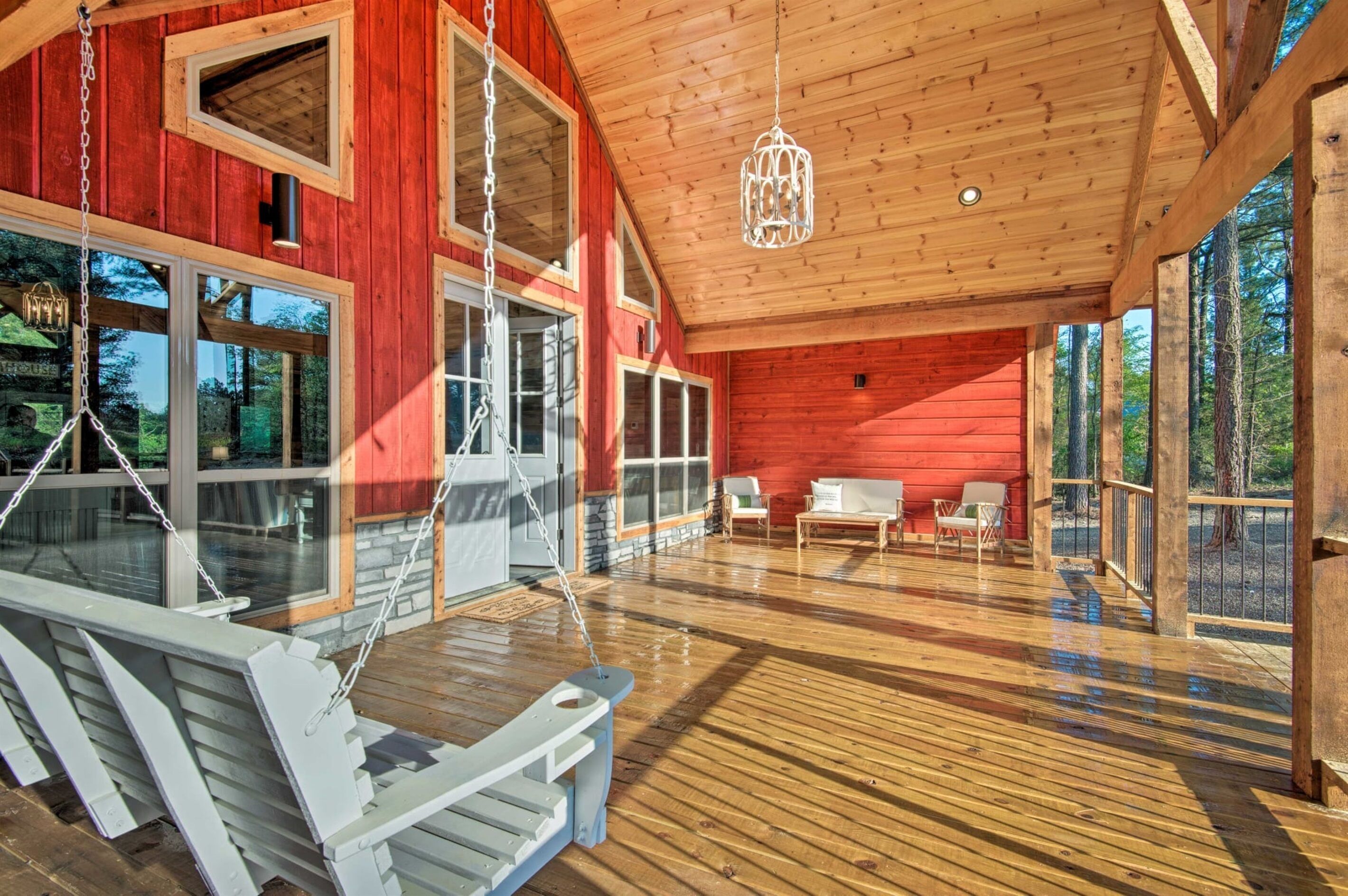 Une vaste terrasse en bois dotée d’une chaise suspendue et d’un luminaire suspendu.