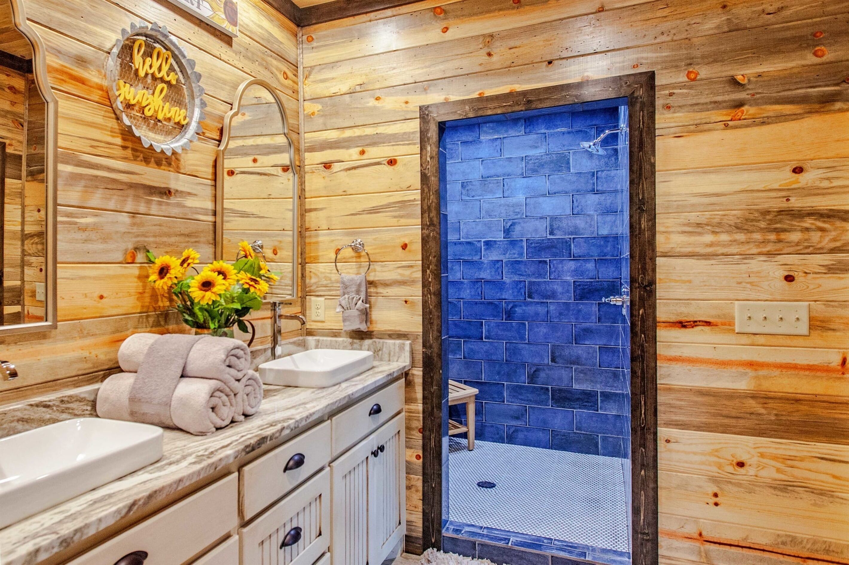 Ein Badezimmer einer Holzhütte mit Waschbecken, Spiegel und einer Duschkabine mit blauen Fliesen.