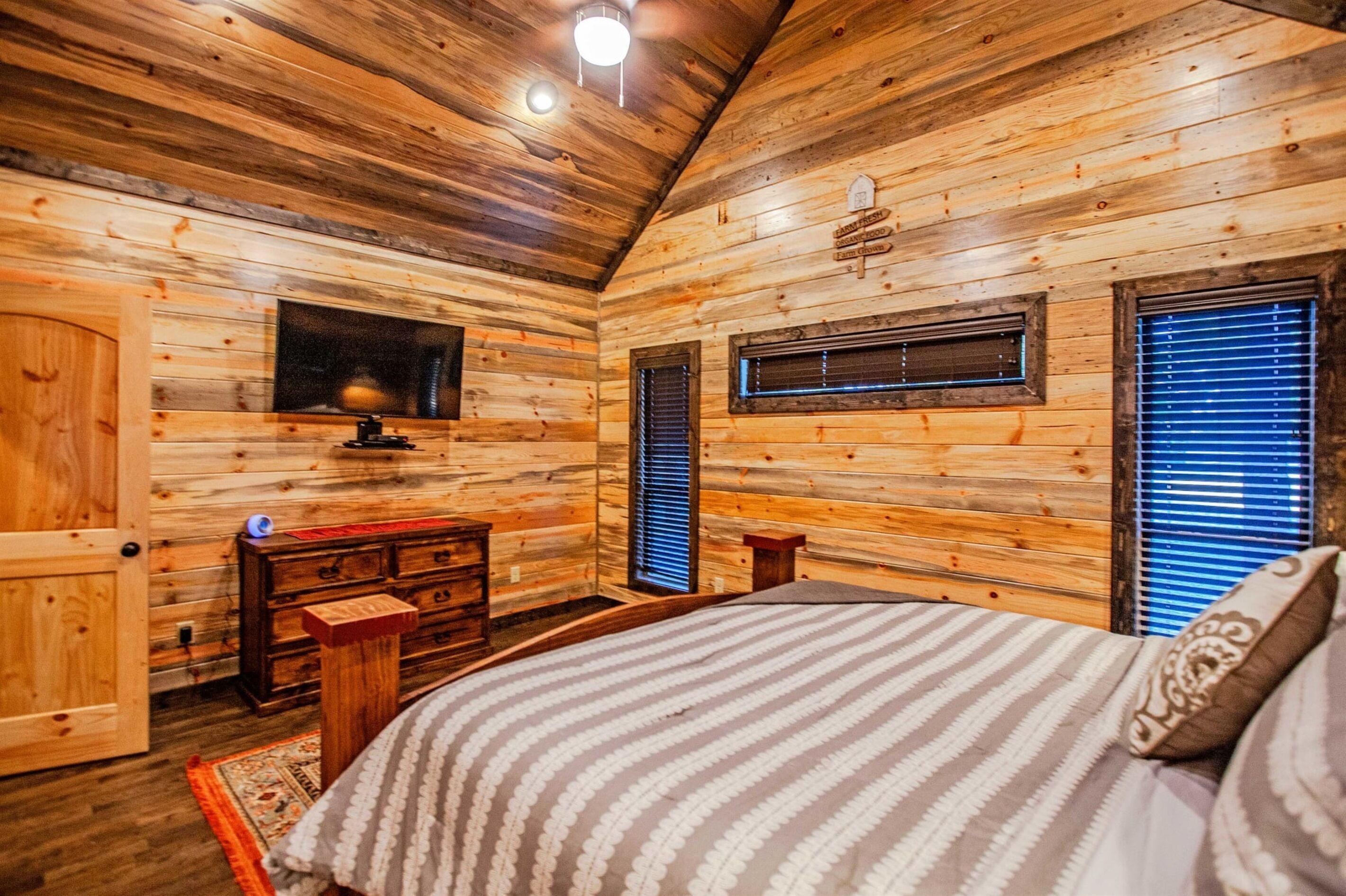 A wooden cabin bedroom with a bed, dresser, and a small window.