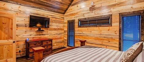 A wooden cabin bedroom with a bed, dresser, and a small window.