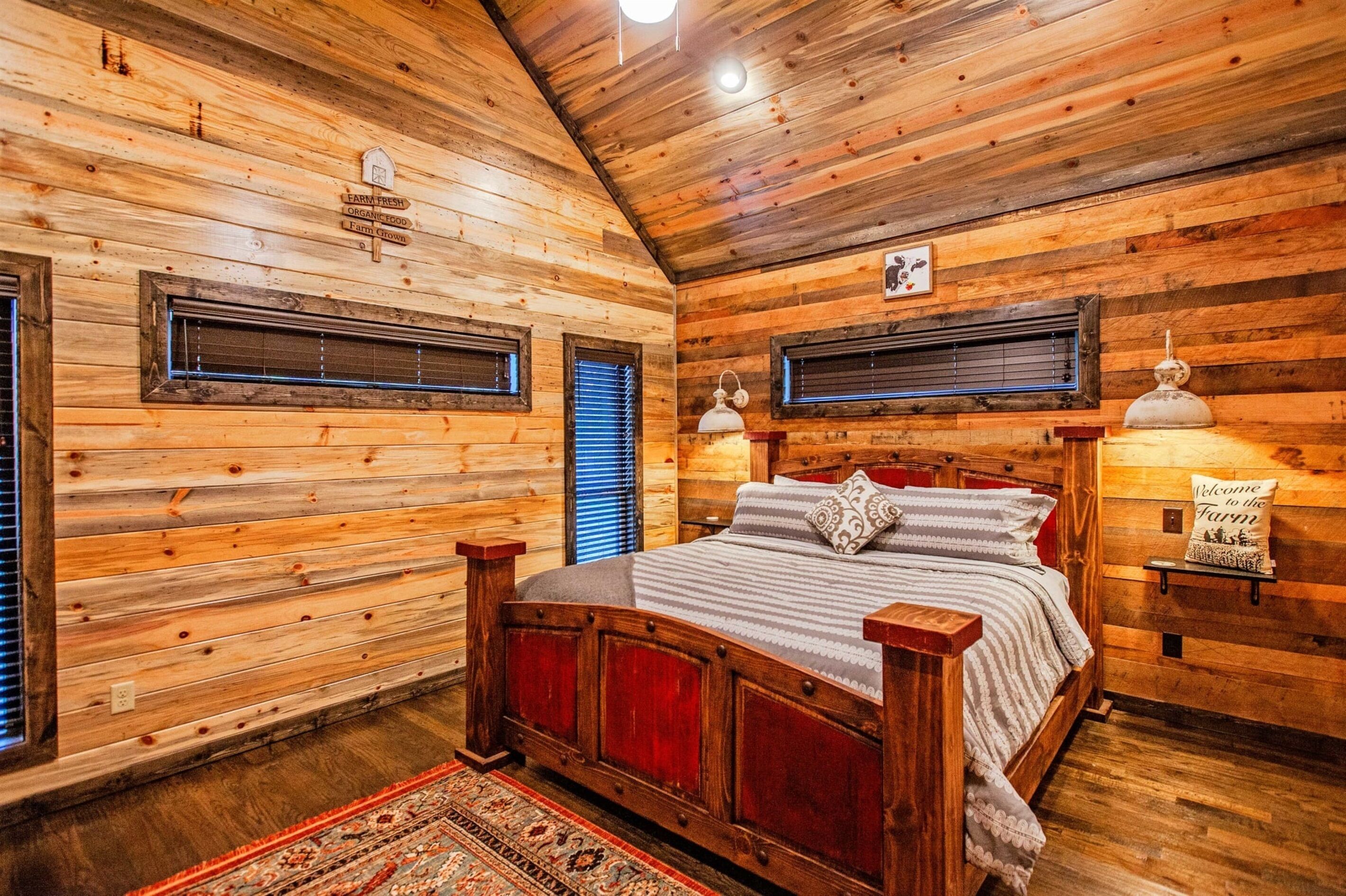 Un dormitorio de cabaña de madera con una cama, dos lámparas de pared y un cartel de bienvenida.