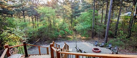 A wooden deck with outdoor seating and a fire pit, surrounded by a forested area.