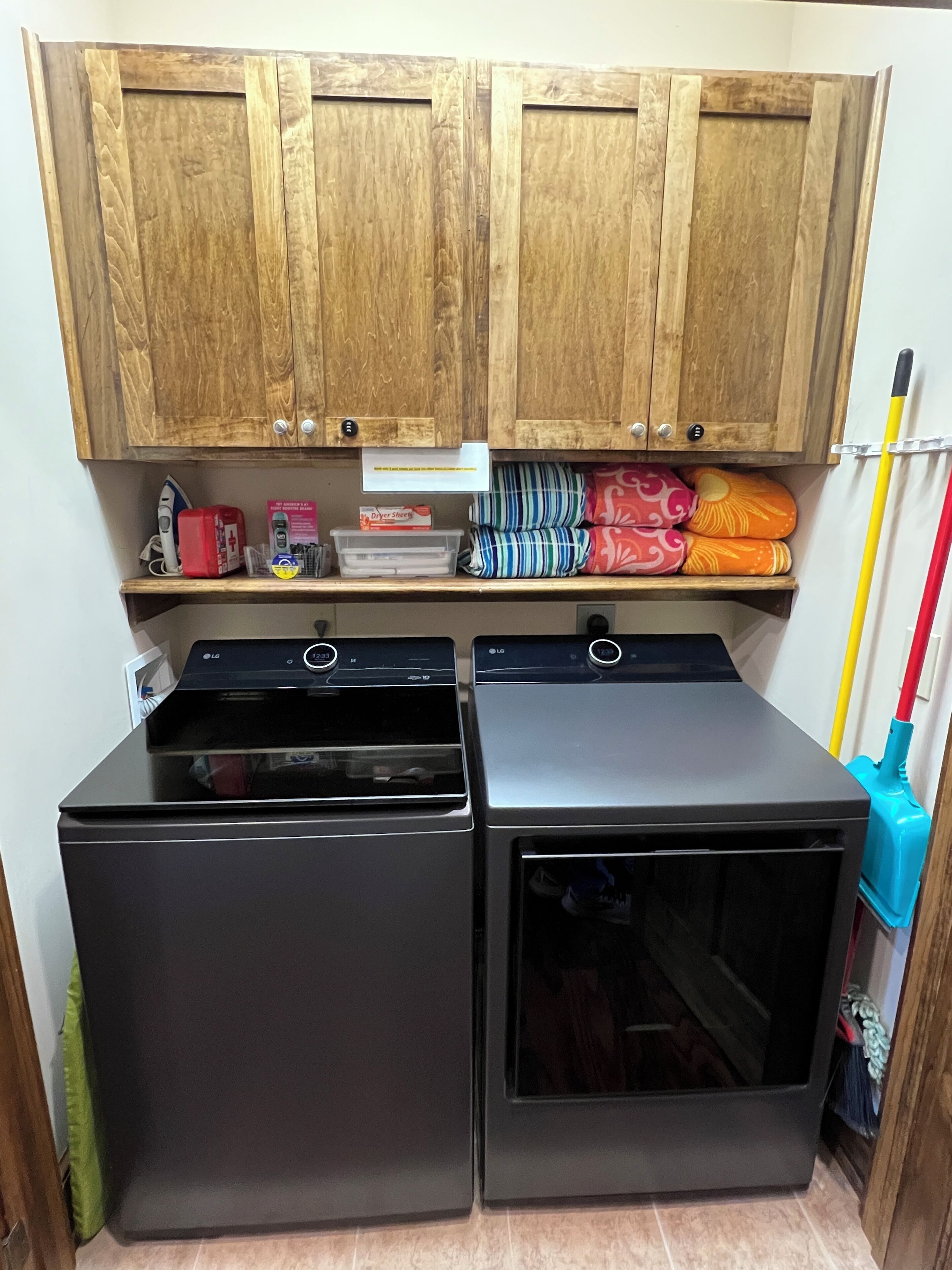 A compact kitchen with wooden cabinets, a built-in washer and dryer, and a small shelf with various items.