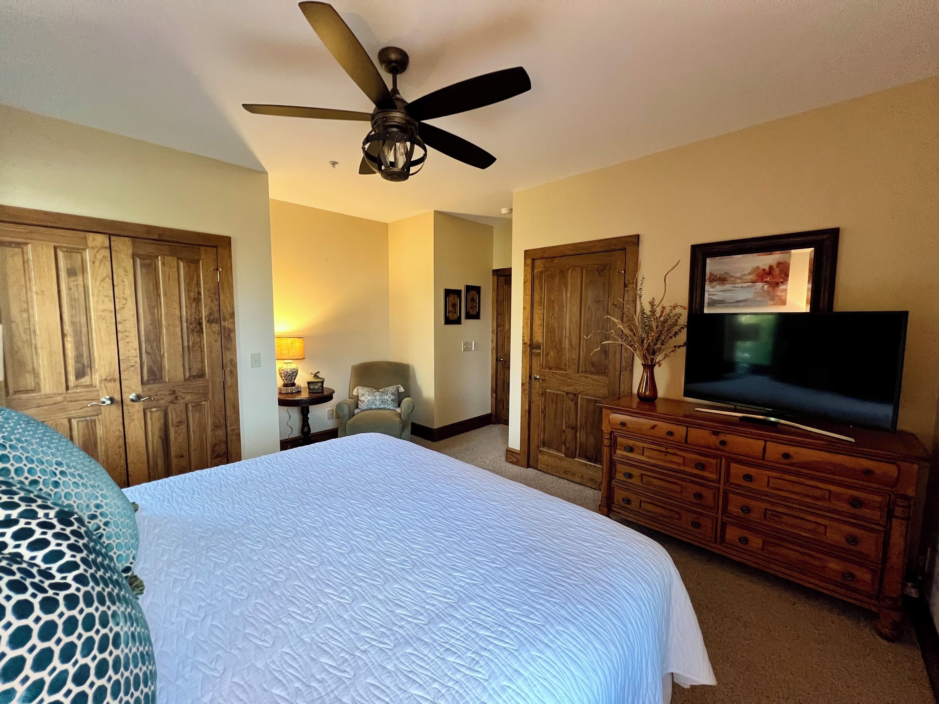 A hotel room with a large bed, a wooden dresser, a television, and a ceiling fan.