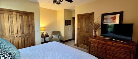 A hotel room with a large bed, a wooden dresser, a television, and a ceiling fan.