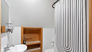 Ein kleines Badezimmer mit einer Holzhilfe, einem weißen Waschbecken und einem gestreiften Duschvorhang.