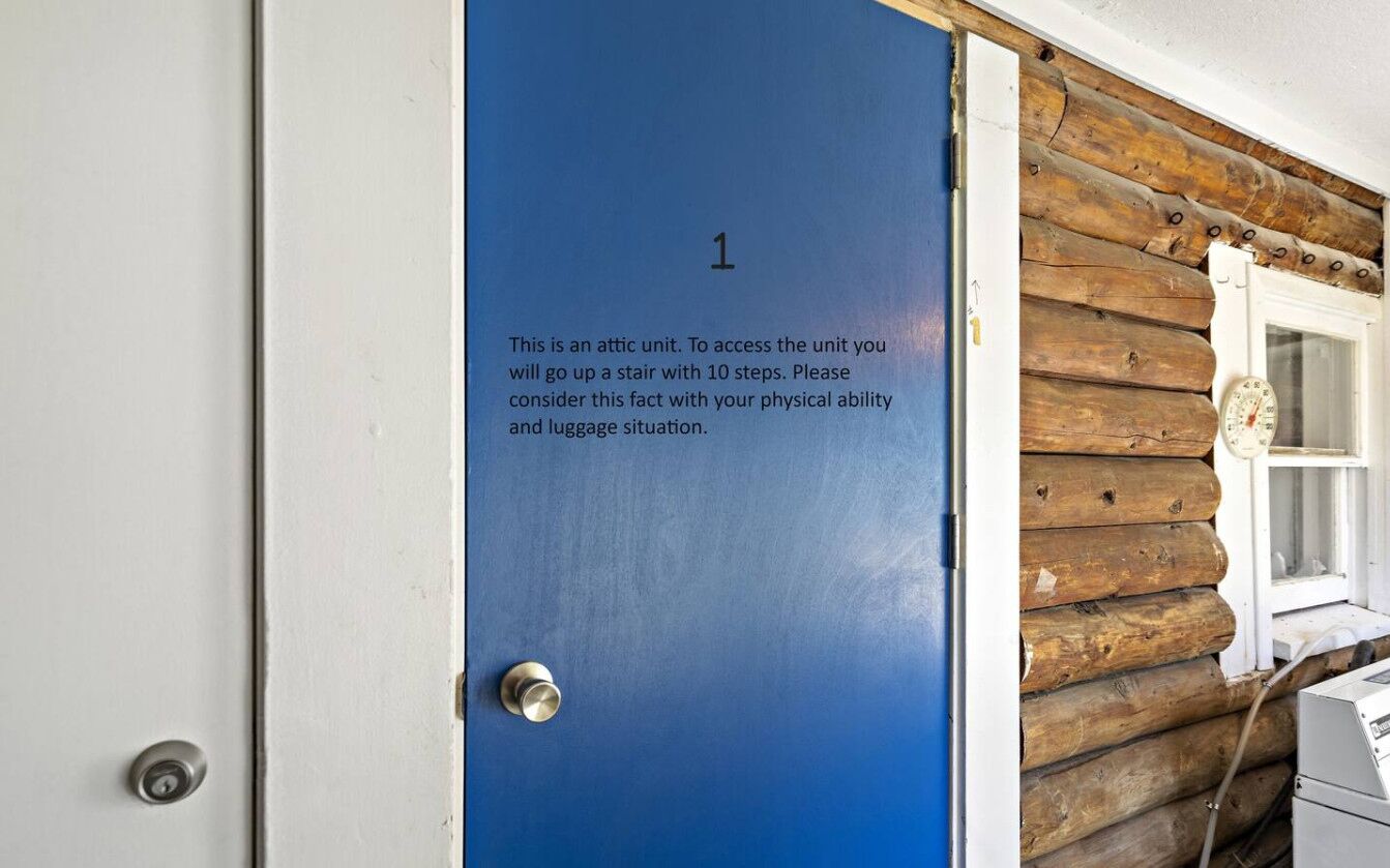 A blue door with a note advising that the unit is an attic and access requires climbing a 10-step stairway.