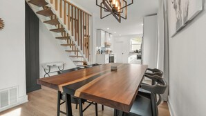 Un espace repas moderne avec une longue table en bois, des chaises noires et un escalier avec des marches en bois.