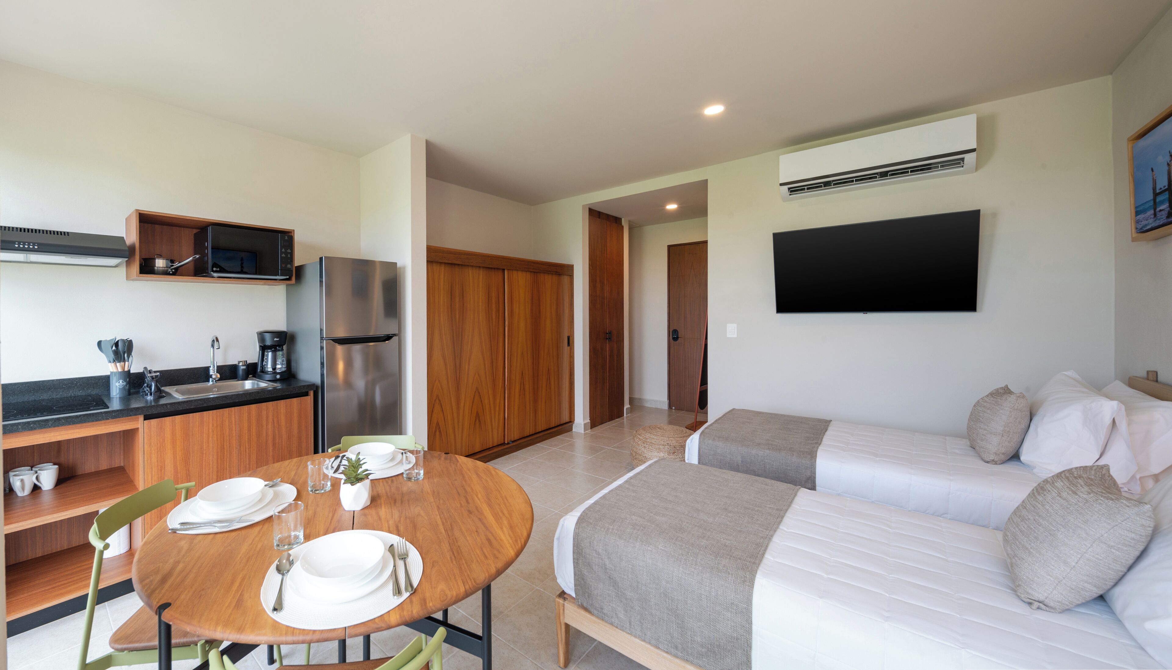 A modern hotel room with a kitchenette, a dining area, and a bed with two pillows.