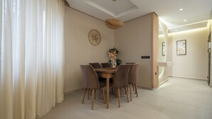 Un comedor con una mesa redonda, sillas, un florero con flores, un reloj de pared y una lámpara de techo tejida.