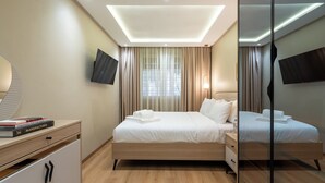 Una habitación de hotel moderna con una cama grande, mesitas de noche, un televisor de pantalla plana y un espejo.