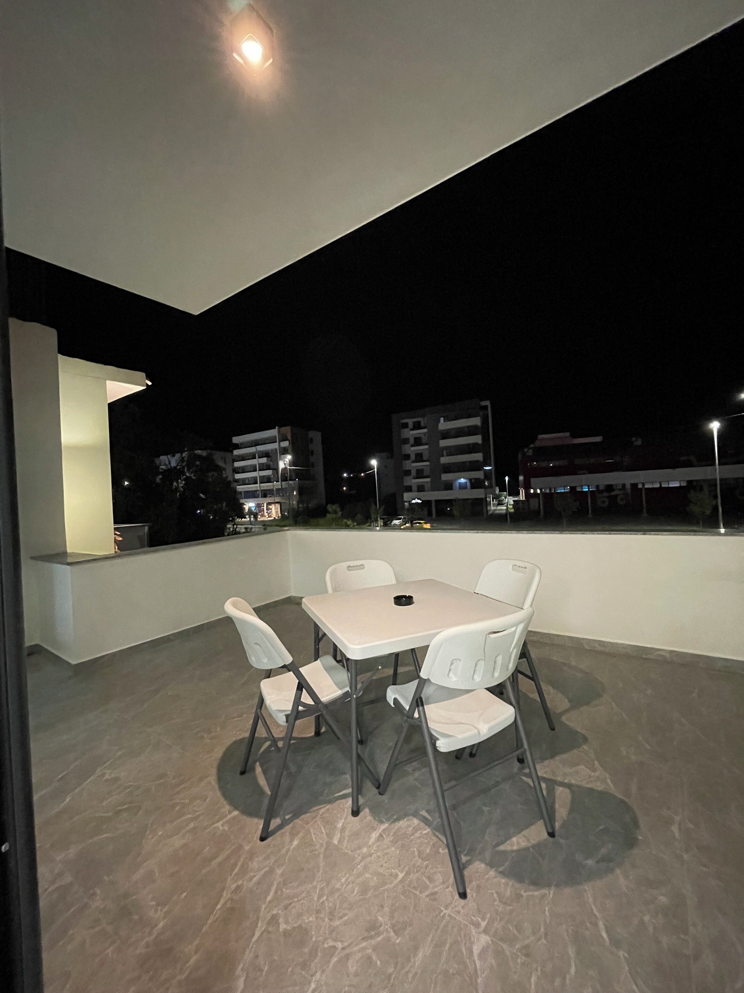 An outdoor patio with a table and chairs, a light fixture, and a view of buildings in the background.