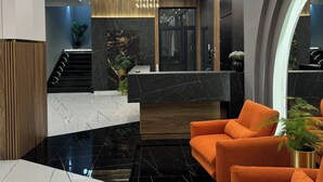 A modern lobby with a marble reception desk, a staircase, and orange seating.