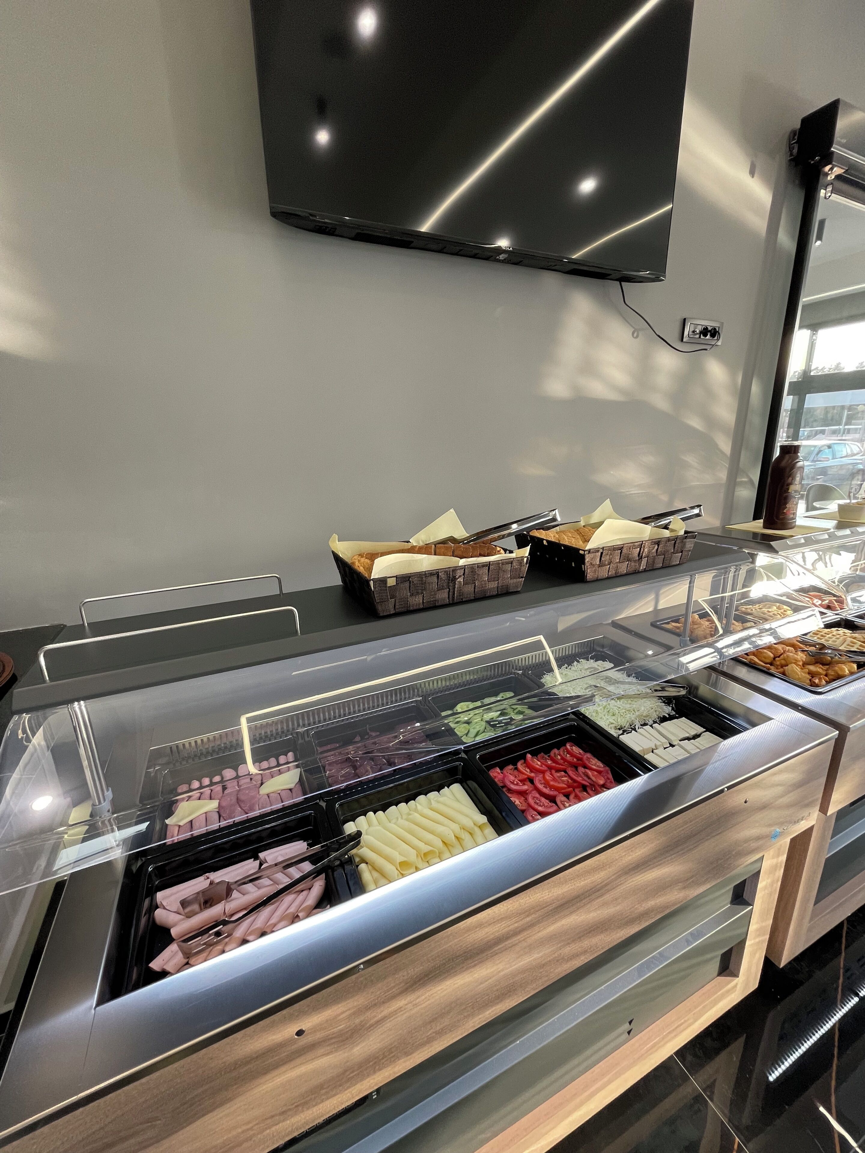 A buffet with various food items, a television mounted on the wall, and a window with natural light.