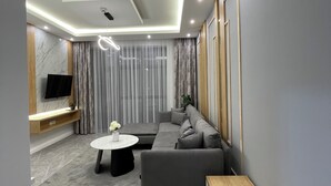 A modern living room with a grey sectional sofa, a round coffee table, and a flat-screen TV mounted on a wooden shelf.