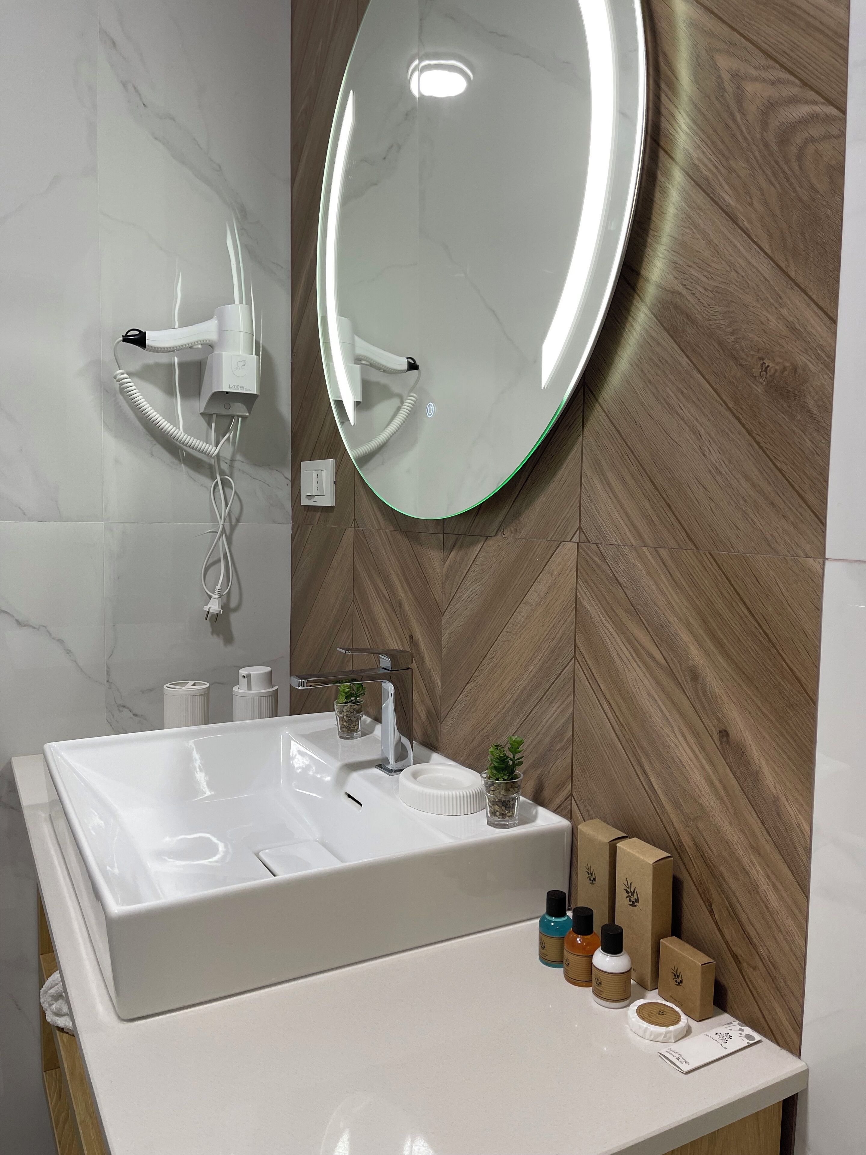 A modern bathroom with a large mirror, a white sink, and a wooden wall.