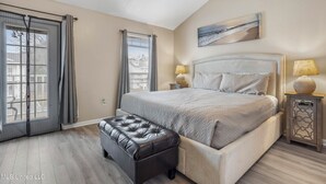 A bedroom with a large bed, a bench, two bedside tables, and a window with curtains. - Sunset Beach Hideaway (Gulfport)