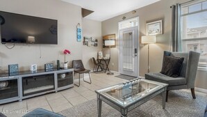 A modern living room with a flat-screen TV, a glass coffee table, a grey sofa, and a ceiling fan. - Sunset Beach Hideaway (Gulfport)