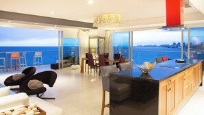 A modern living room with a large glass wall, a dining area, and a kitchen with a black countertop. - Lujoso Peninsula T3 Frente al Mar (Puerto Vallarta)