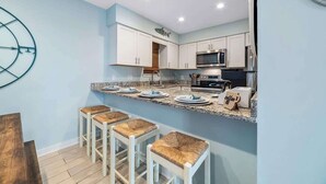 A modern kitchen with white cabinets, a granite countertop, and a coffee bar. - Affordable updated 2BR family retreat with pool (Gulf Shores)