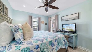 A bedroom with a bed, a ceiling fan, a TV, and a view of the outside. - Affordable updated 2BR family retreat with pool (Gulf Shores)