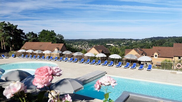 A pool area with lounge chairs and umbrellas, surrounded by buildings and trees.