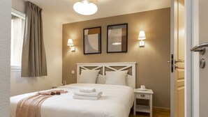 A neatly made bed with white linens and a folded towel, a bedside table with a cup, and two wall-mounted lamps.