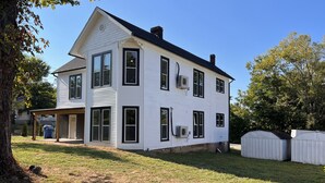 Une maison blanche à deux étages, dotée d’un porche abrité, de nombreuses fenêtres et d’une cour clôturée.
