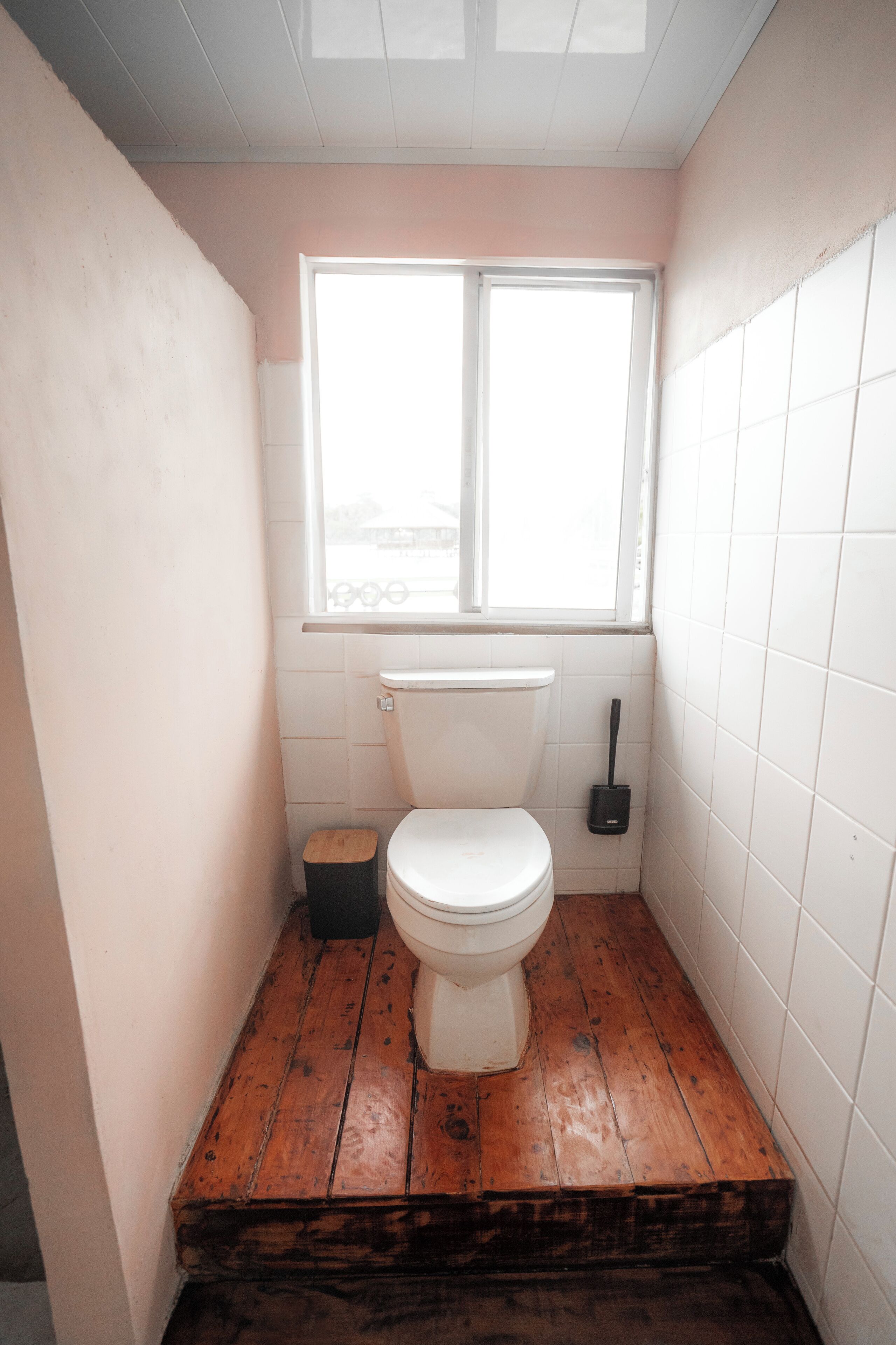 A small bathroom with a toilet, a window, and a wooden floor.