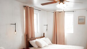 Une chambre avec deux lits, des têtes de lit en bois, un ventilateur de plafond et une fenêtre avec des rideaux.