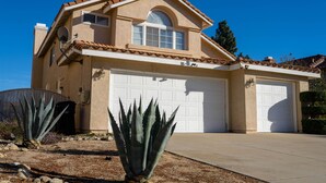 Une maison à deux étages avec un garage, une antenne parabolique et de grands plants d’agave dans le jardin.