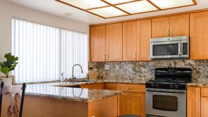 Une cuisine avec des meubles en bois, un plan de travail en granit, une cuisinière en acier inoxydable et un four à micro-ondes.